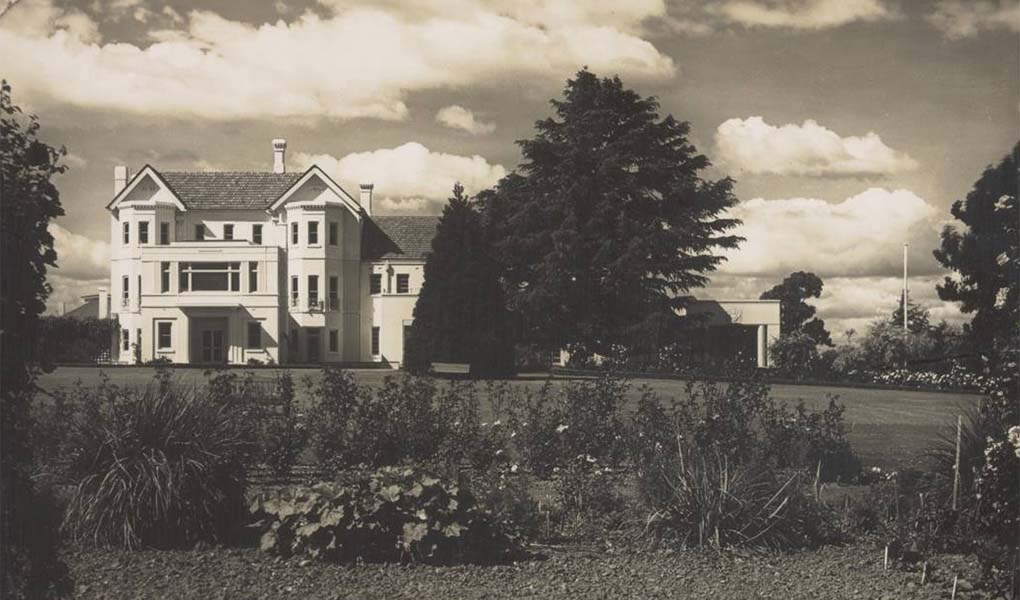 A sepia toned photographic postcard of a grand white building in sweeping gardens.