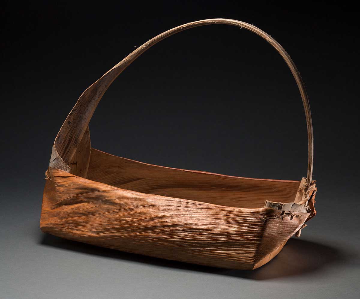 A rectangular shaped basket with a handle made of natural fibres. The handle has other natural fibres beige in colour wound around it.