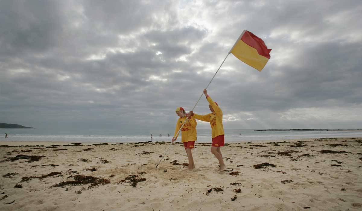Two surf lifesavers putting a red and yellow flag on the beach at Mollymook, New South Wales, 2006.