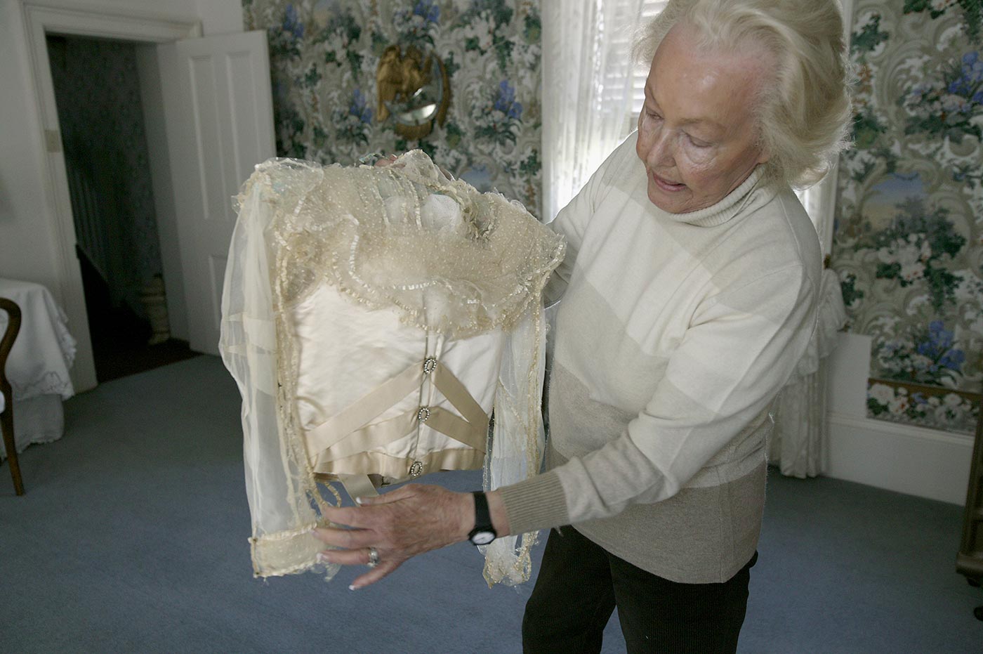 A woman stands in room holding and inspecting the back of a wedding dress bodice.