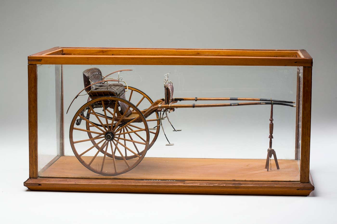 A small model wooden sulky in a timber and glass display case.