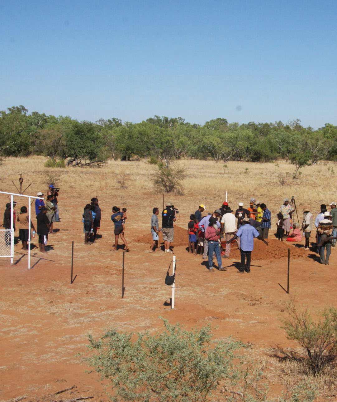 Photo of a group of people observing and filming a burial ritual.