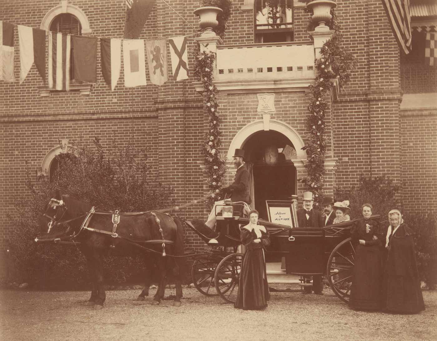 Sepia coloured photograph showing a landau carriage pulled by a horse standing in front of the homestead entrance with the honeymoon couple being greeted by relatives.