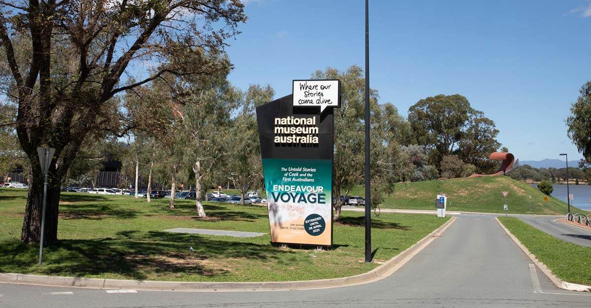Entrance to the National Museum of Australia carpark with a large sign on the left advertising a major exhibition.