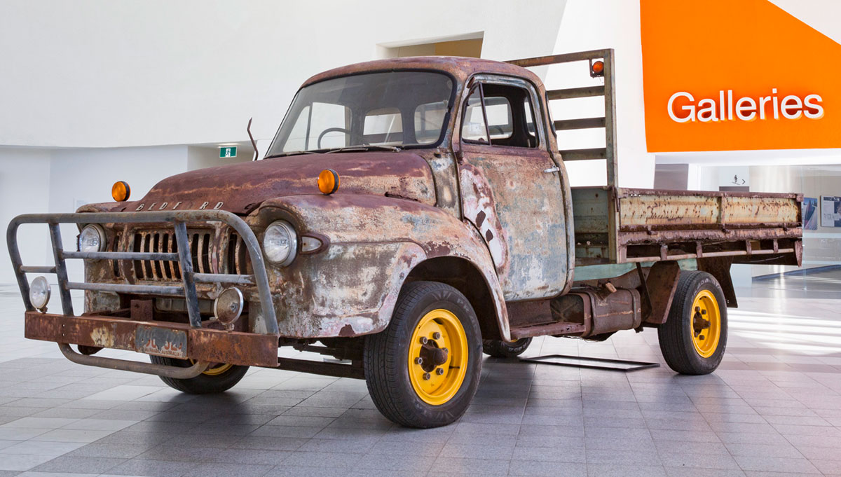 An old flatbed truck with rusted exterior and fitted with a bullbar on the front.