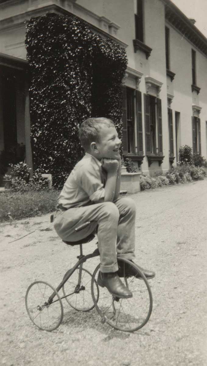 A black and white photo of Andrew Gibson as a child sitting on his tricycle.
