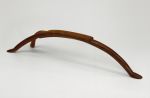 Headrest kali Headrest made of a hard wood and used as a pillow. A semi-circular piece with a flat, rectangular upper surface. One side forms one leg and the other divides into two legs.