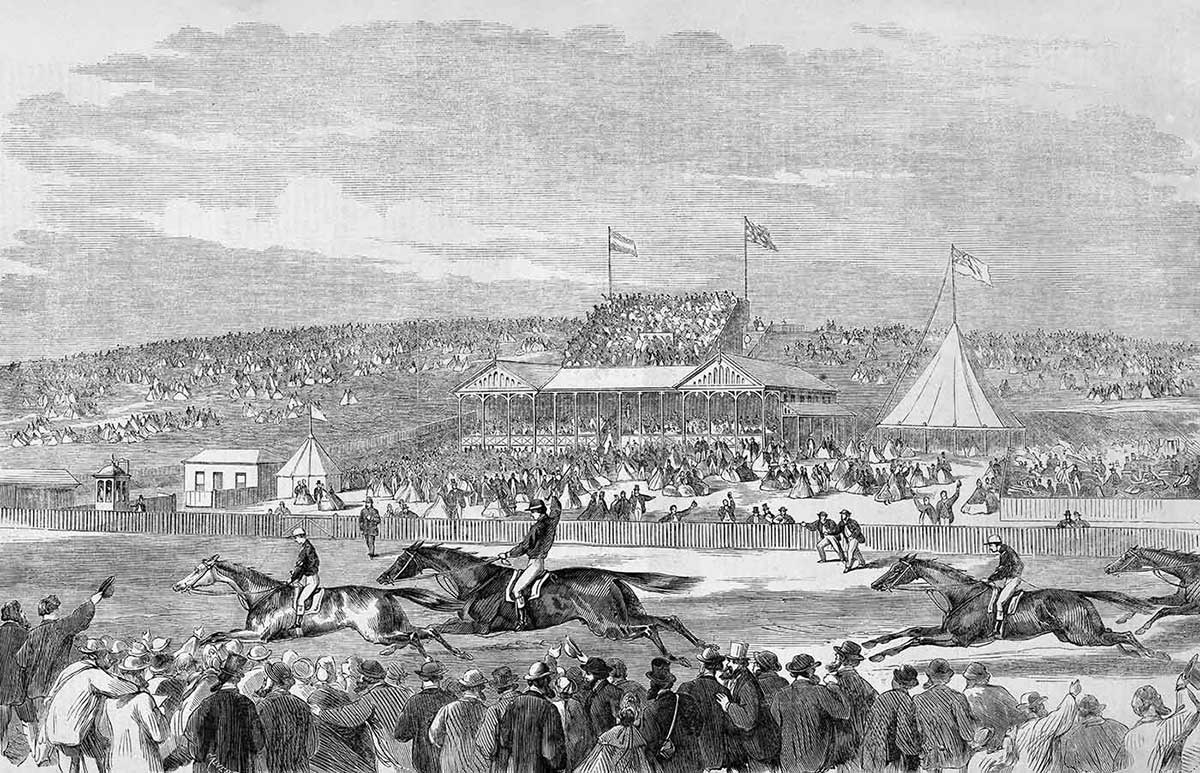 Black and white print showing four horses being ridden by jockeys on a track. Large crowds of people stand on either side of the track, with pavilions and flags visible in the distance.