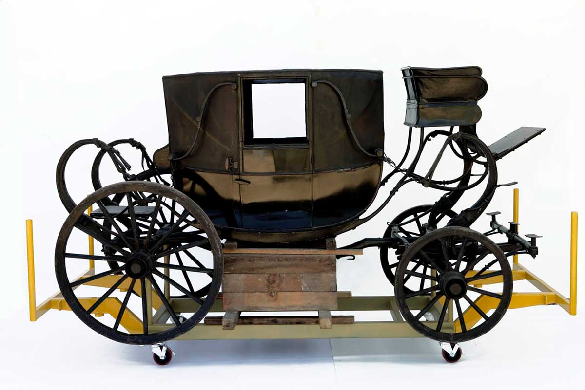 Wooden horse-drawn coach, painted black, with four wheels and mudguards, and Coachman seat at front.