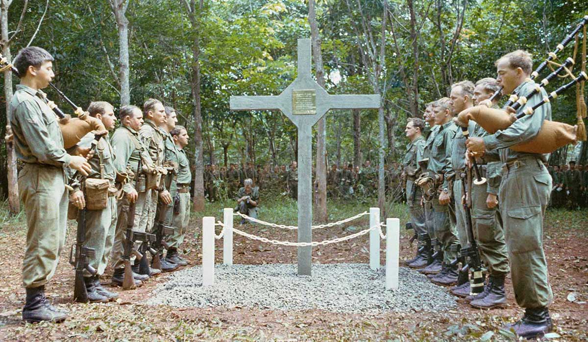 Soldier in formal procession around a cross-shaped memorial.