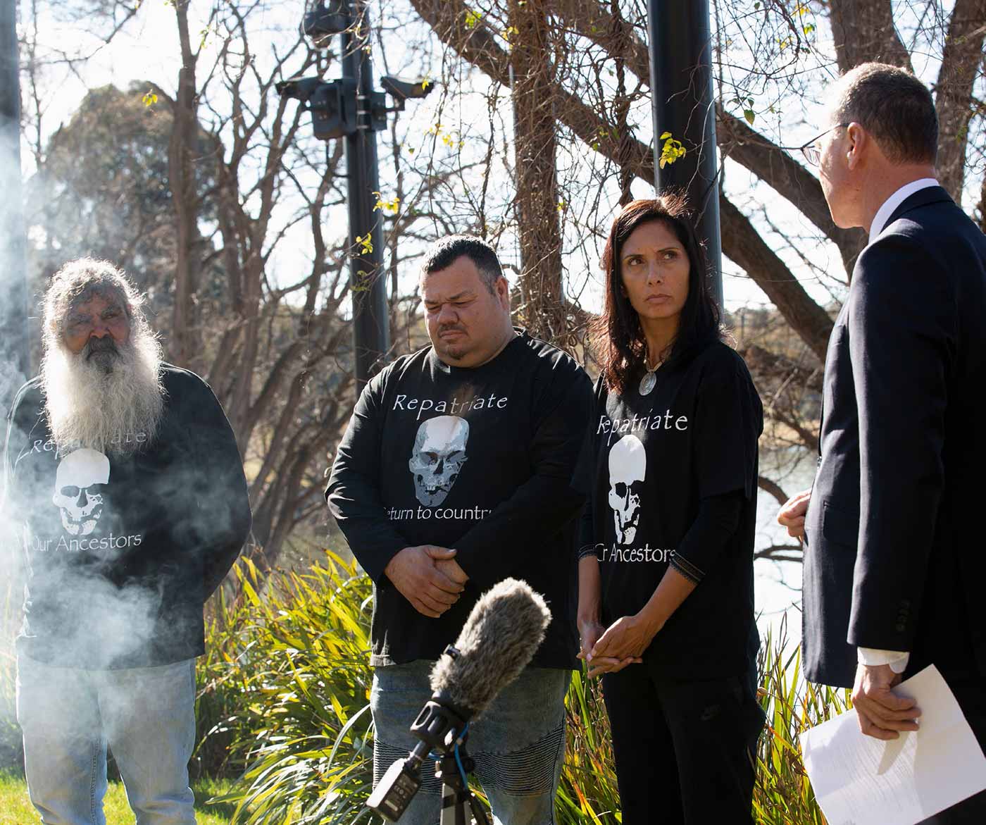 Photo of four people standing in the garden surrounded by smoke and media equipment.