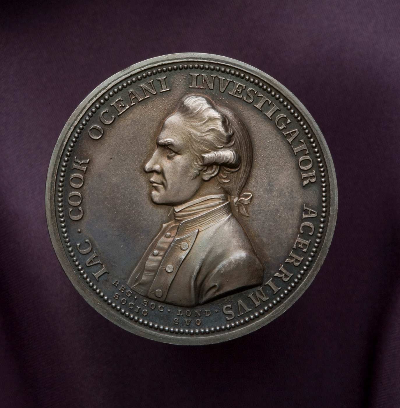 A solid copper medal with a bronzed patina, which features on the obverse a profile portrait bust of Captain James Cook in uniform, and on the reverse Fortune leaning upon a column with a spear in the crook of her arm, holding a rudder on a globe. Encircling the portrait of Cook is the Latin text