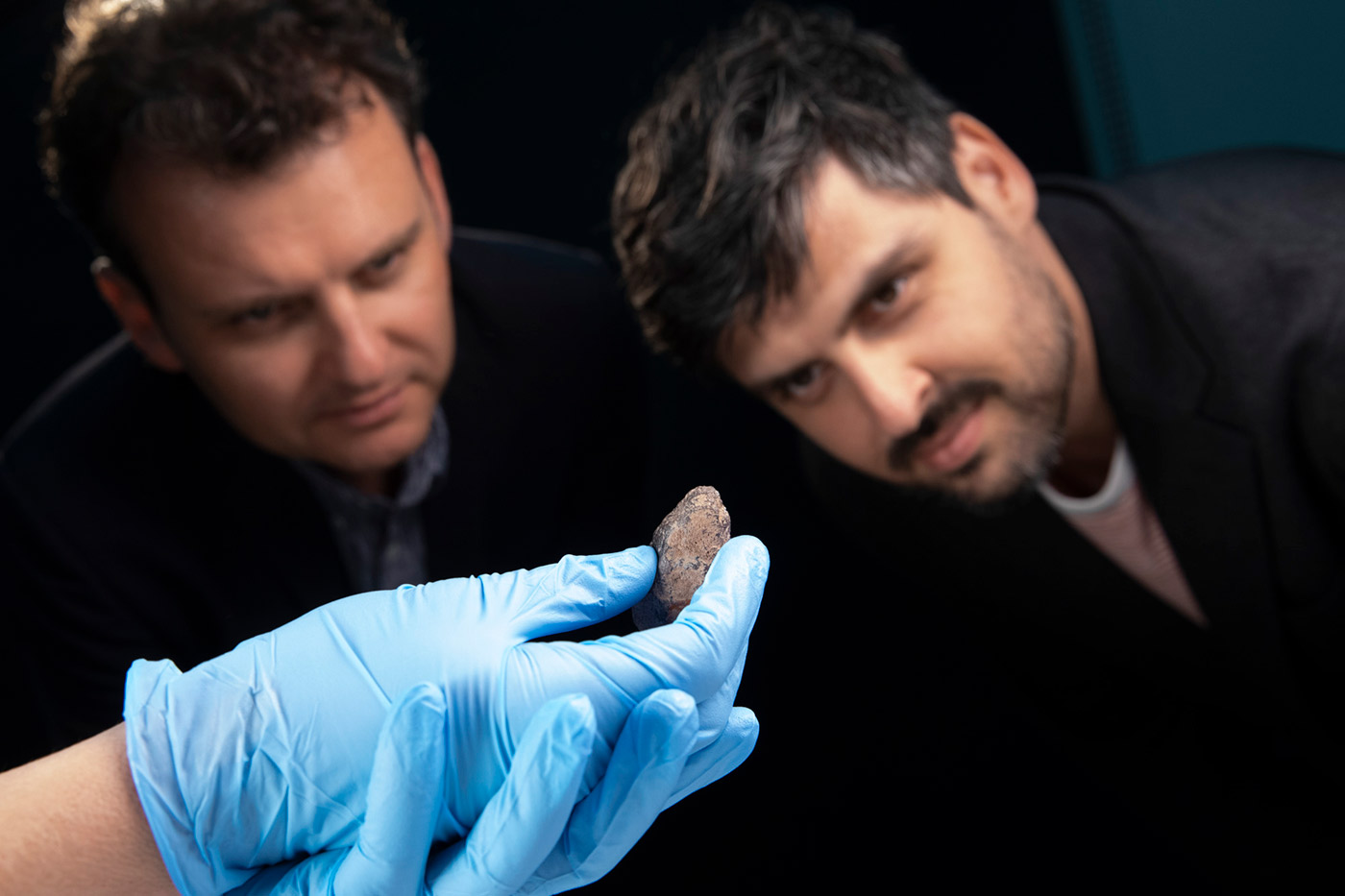 Slava and Leonard Grigoryan inspect a small piece of ochre being held in hand wearing conservation gloves.