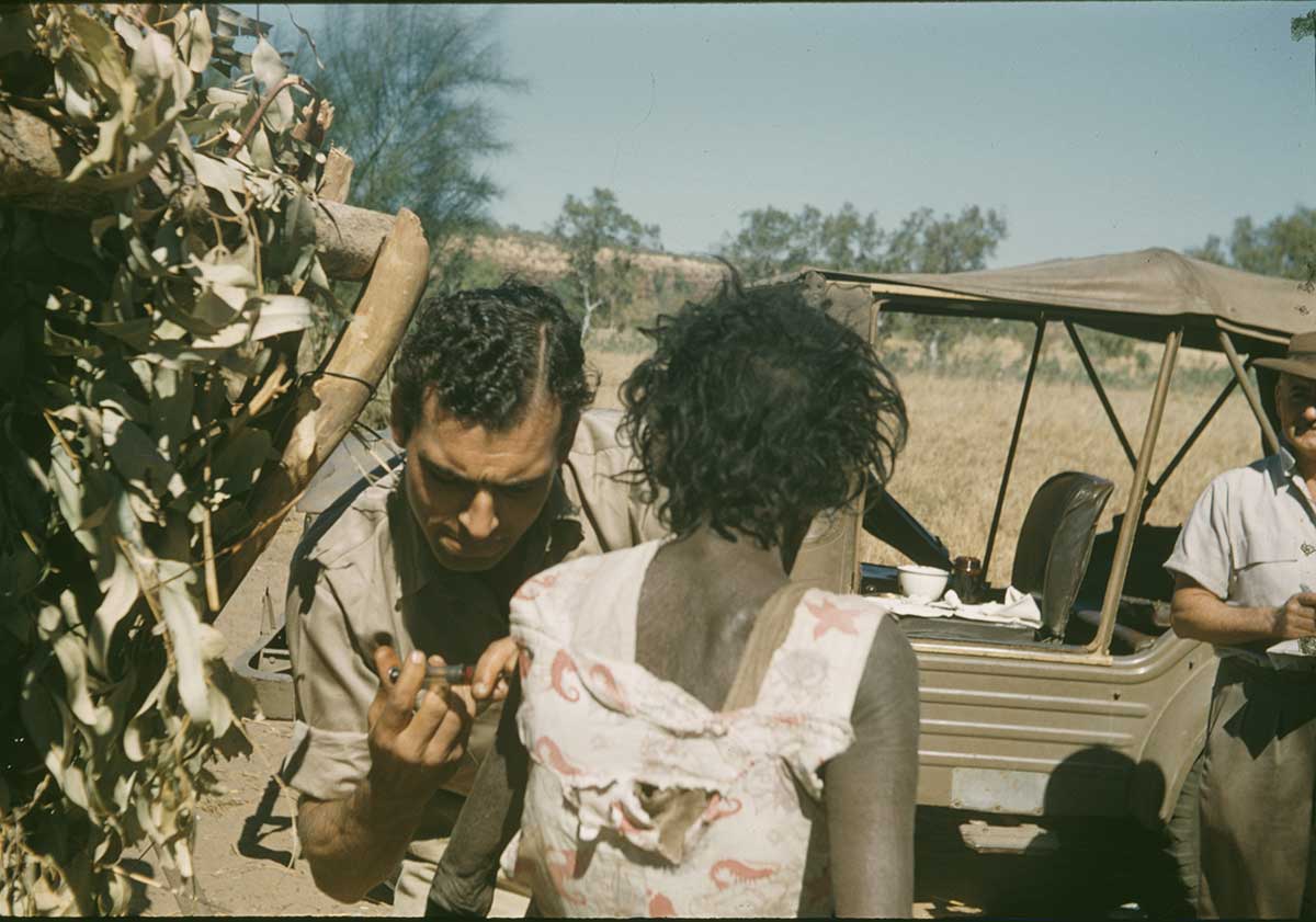 Coloured photograph of a medical practitioner injecting a needle into a woman’s arm.