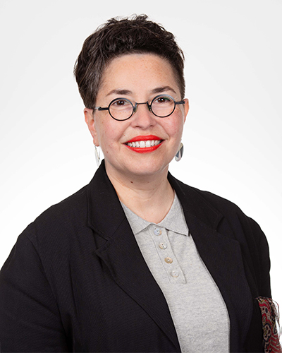 Portrait of Esther Anatolitis. Esther wars a grey shirt and black jacket and glasses.