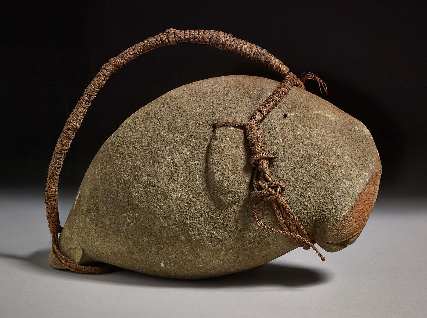 Dugong shaped from grey stone with a cord for suspension and a red ochre strip along the backbone.