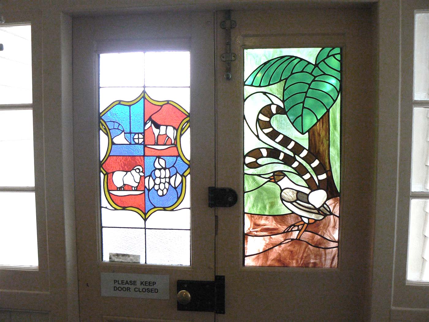 Leadlight windows featuring a design in the style of a coat of arms on one side and a forest scene with a bird on the other.