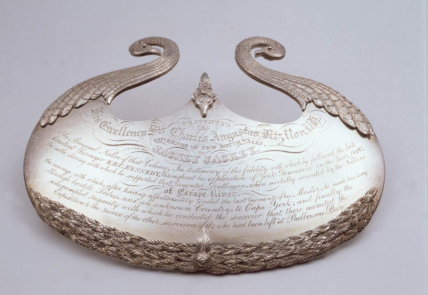 Silver gorget with ornate engraved design and text.