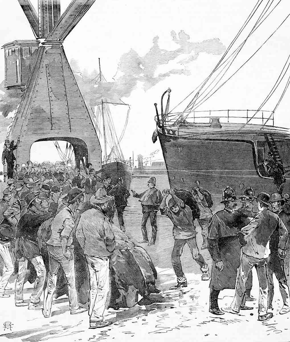 A handful of men carrying sacks from a moored ship surrounded by large numbers of jeering men kept at bay by a handful of police.