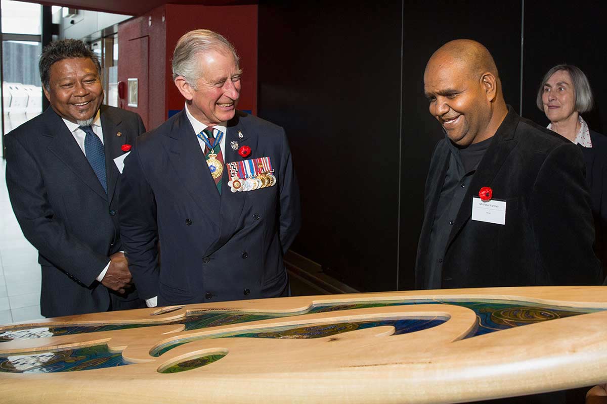 Three men stand behind a timber surfboard with coloured glass inserts.