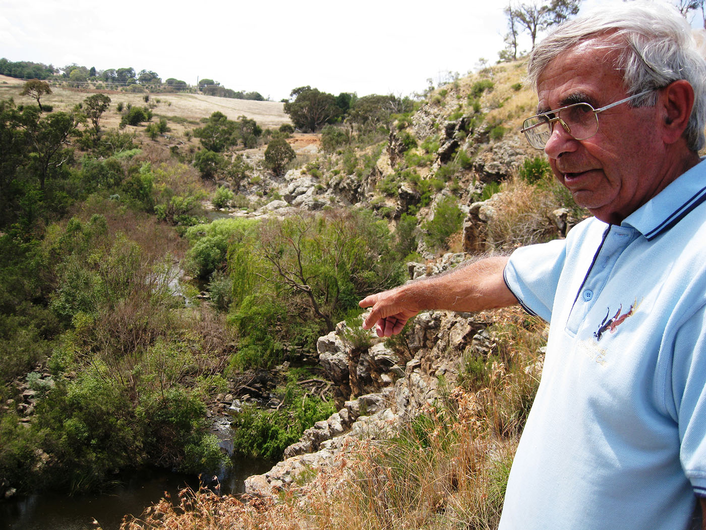 Eric Bell stands on a hillside, pointing to a small river below.