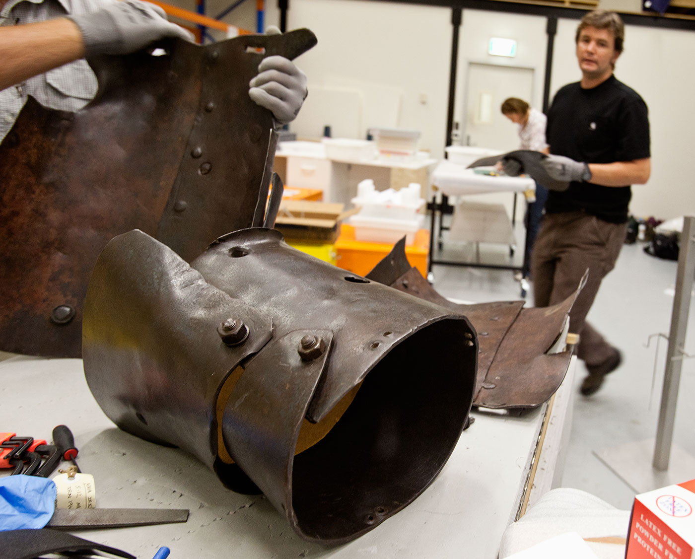 Conservators working on crude looking armour in a workshop.
