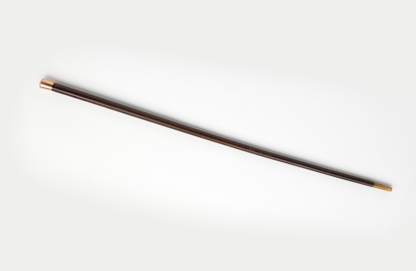 A wooden walking stick with a gold band at the the top and a cardboard tag tied to the stem.