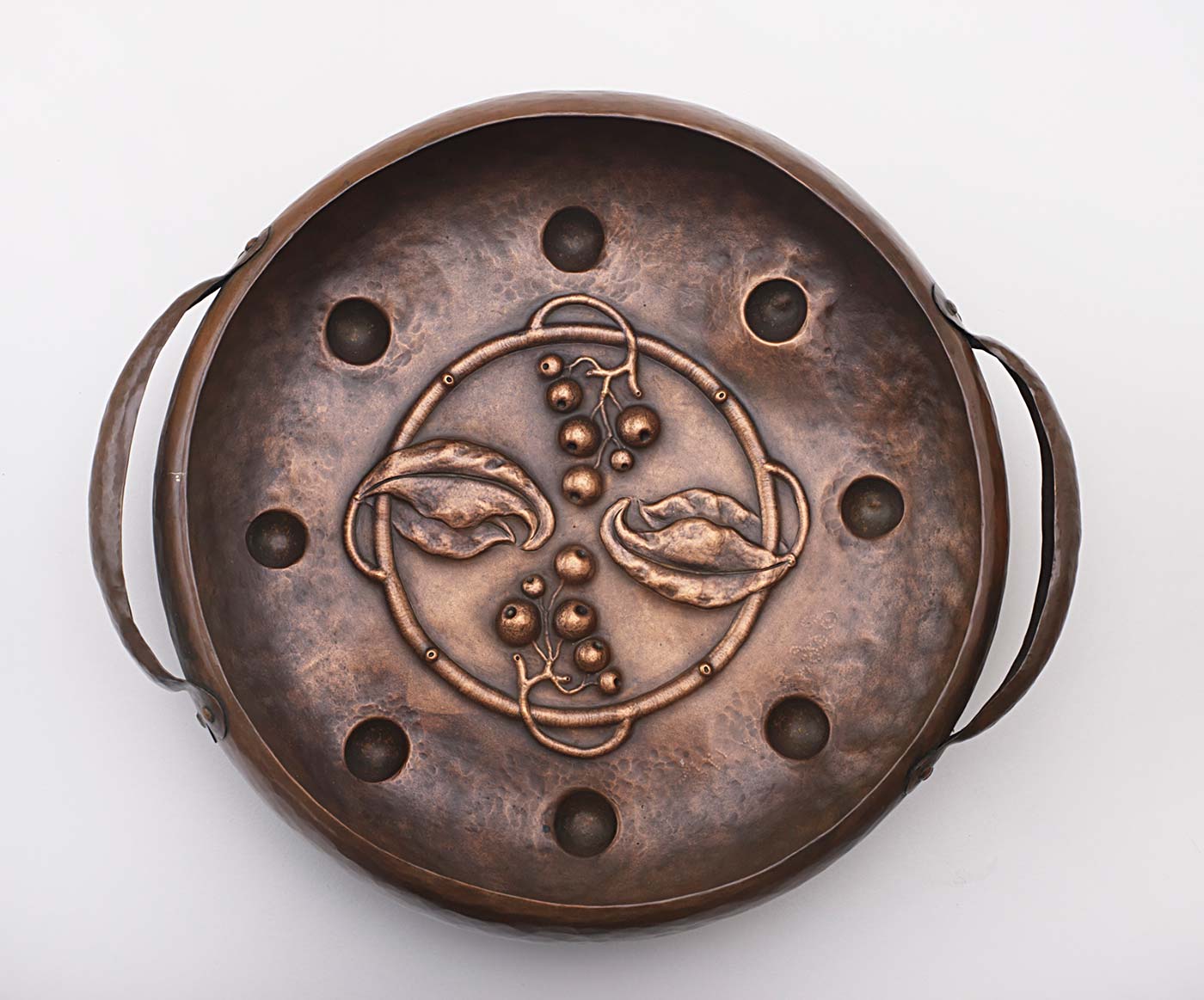 Beaten copper bowl with two handles and a central decoration of leaves and berries.
