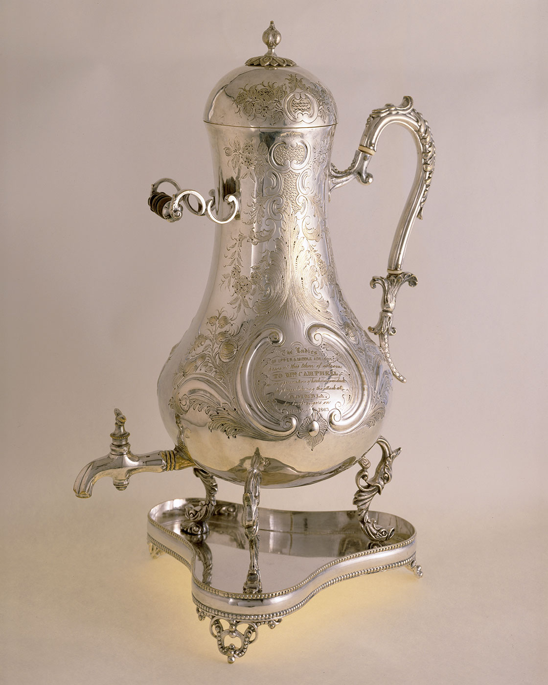 Silver urn on a tray with an ornate design and inscriptions.