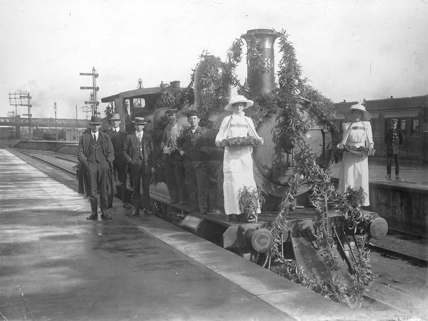 Train engine adorned with plant material. A group of people stand in front of and beside the engine.