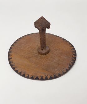 Food suspension hook taunga A food suspension made of flat, round white wood, that suspends from the ceiling. The smooth side of the rim has a pattern with one row of black triangles, each with a zigzag line on top.