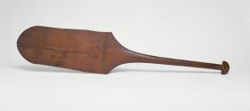 301.jpg Dance paddle made of wood with an almost rectangular and rounded blade and a semi-circular knob at the end of the handle.