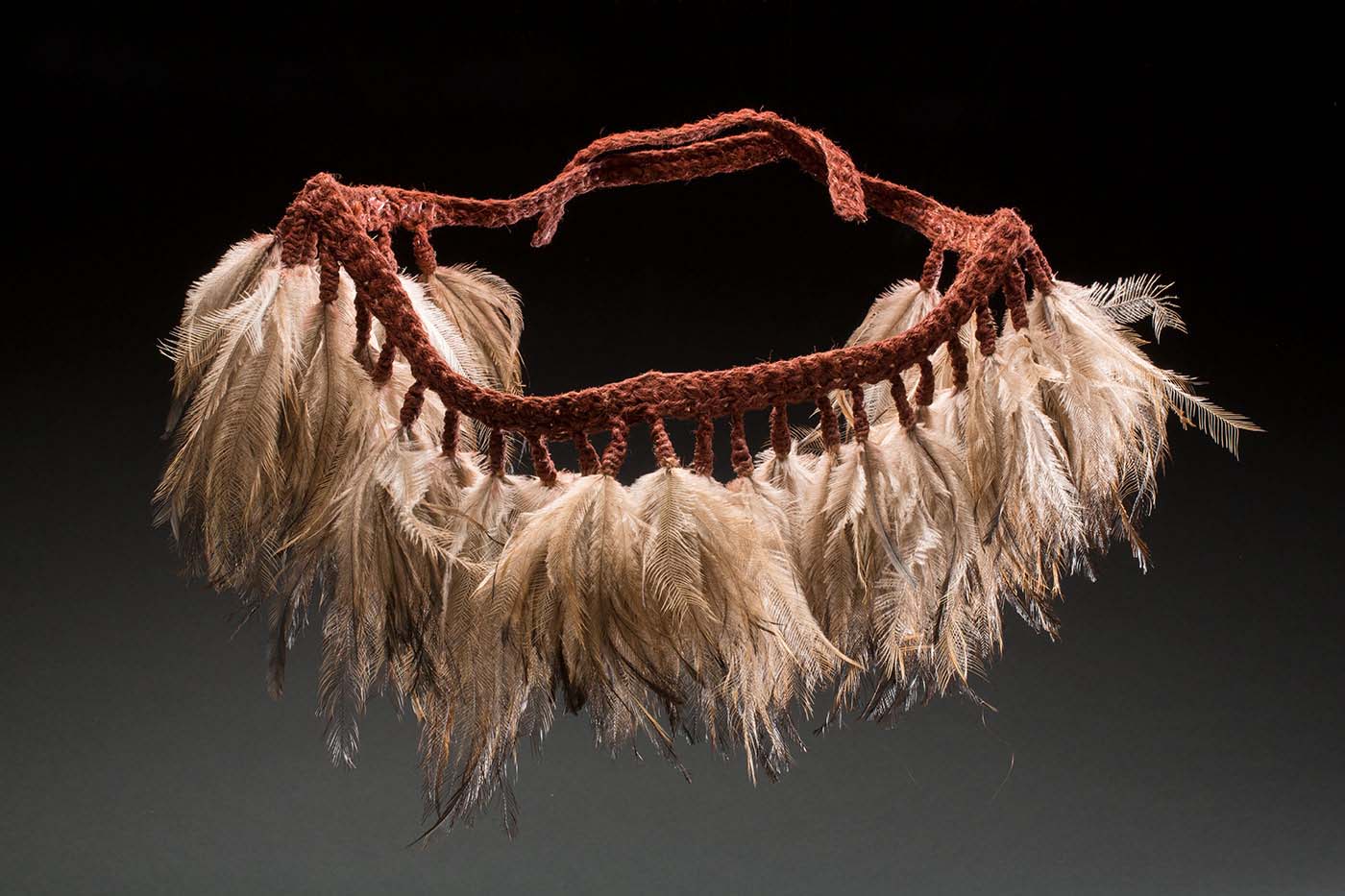 A belt woven from red fibrous material, to which bunches of emu feathers have been attached.to form a skirt.