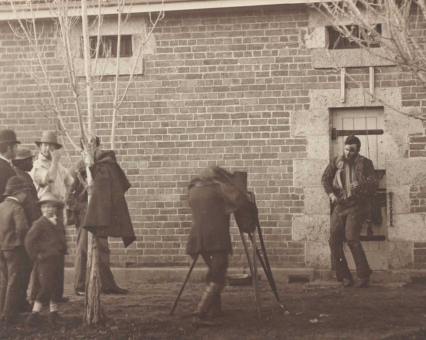 Black and white photo of a filming scene where a man is being filmed with a people looking on.