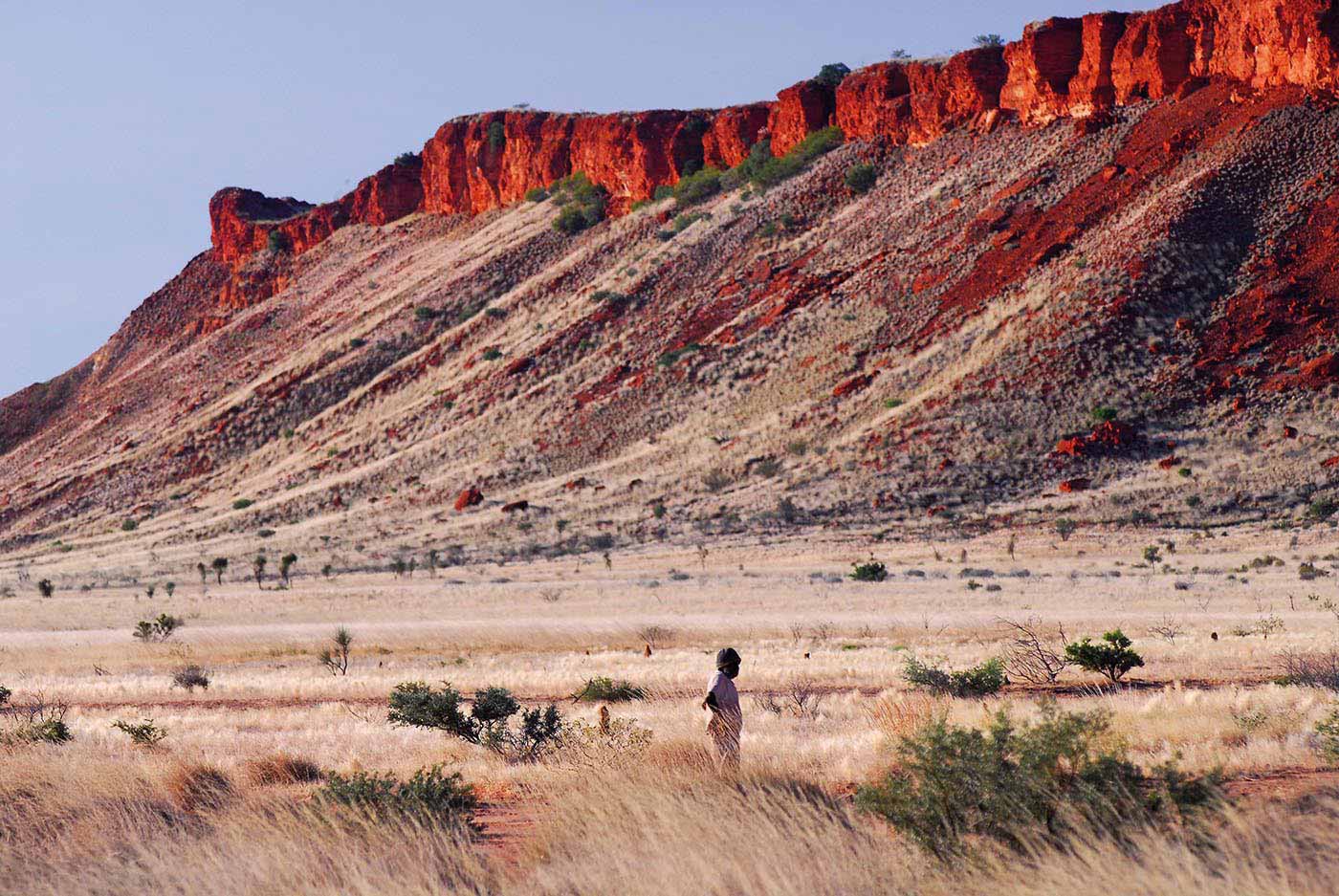 Colour photo of a landscape featuring a sloping mountain tapering to a red rock at the top.